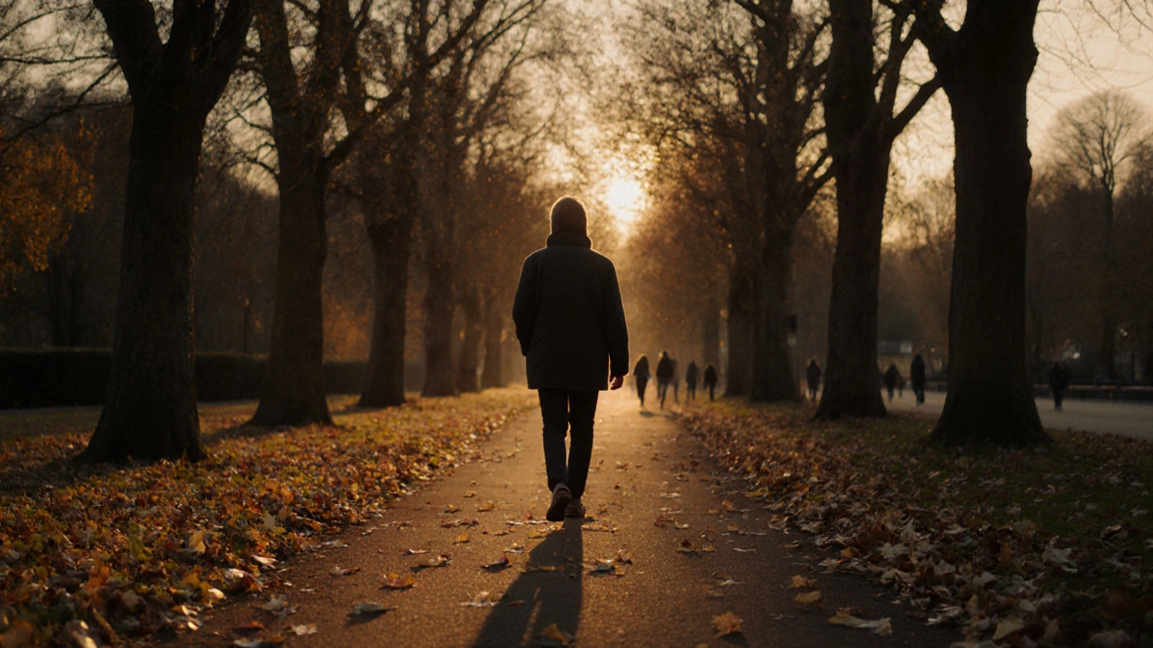 A person walking alone through Hyde Park at golden hour, autumn leaves underfoot.