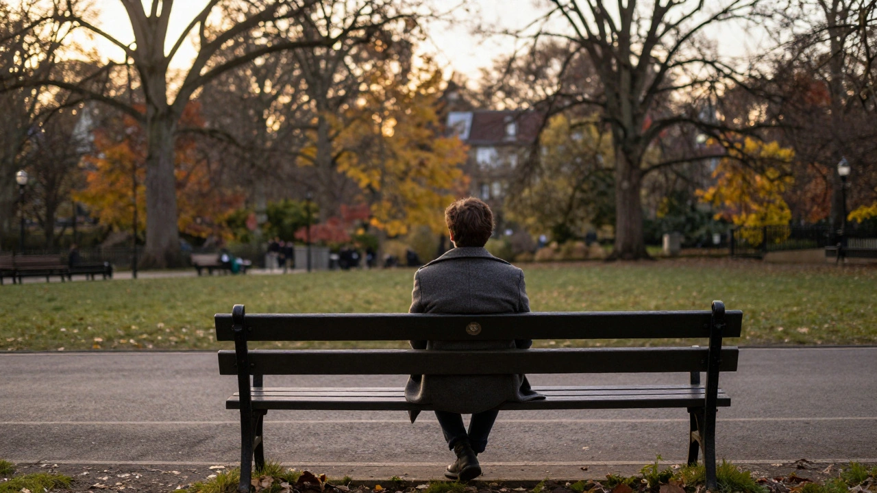 One person sitting alone on a park bench at sunset, coat on, looking out peacefully.